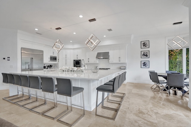 kitchen with built in appliances, a spacious island, white cabinets, and pendant lighting