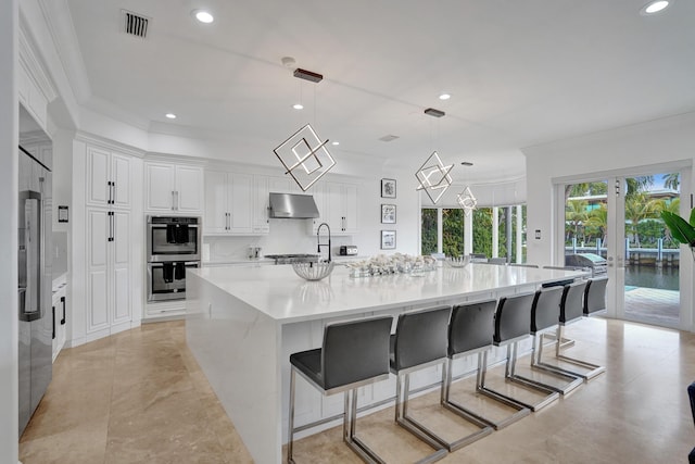 kitchen featuring a large island, double oven, crown molding, pendant lighting, and white cabinets