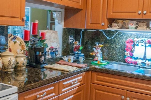 kitchen featuring tasteful backsplash, dark stone counters, and sink