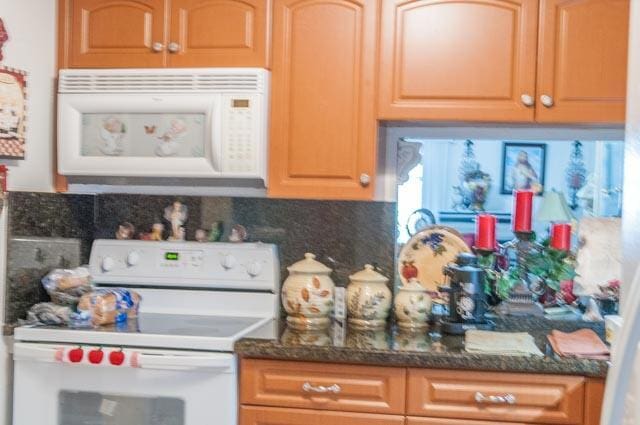 kitchen with dark stone countertops, white appliances, and backsplash