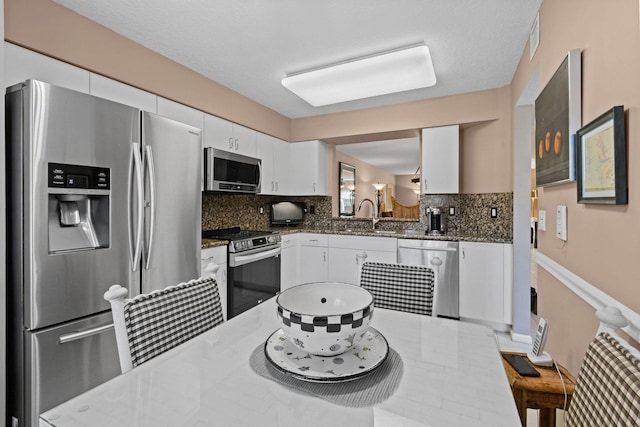 kitchen with white cabinetry, appliances with stainless steel finishes, and dark stone counters