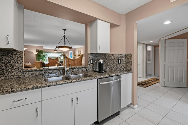 kitchen featuring white cabinets, sink, stainless steel dishwasher, dark stone countertops, and decorative light fixtures