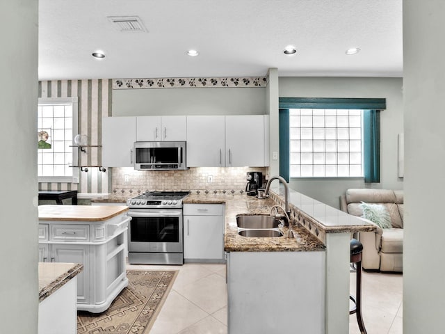 kitchen with white cabinets, sink, a kitchen bar, kitchen peninsula, and stainless steel appliances