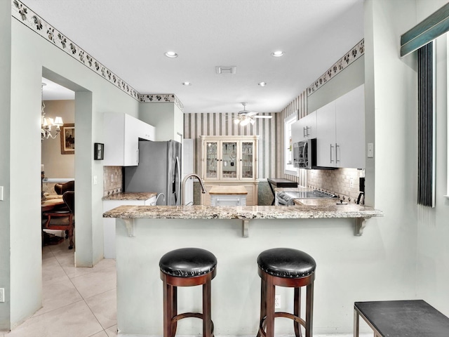 kitchen featuring white cabinets, kitchen peninsula, appliances with stainless steel finishes, and tasteful backsplash