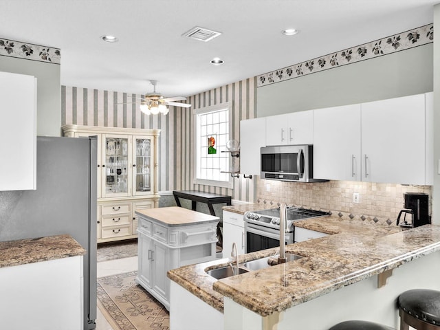 kitchen featuring ceiling fan, sink, kitchen peninsula, white cabinets, and appliances with stainless steel finishes