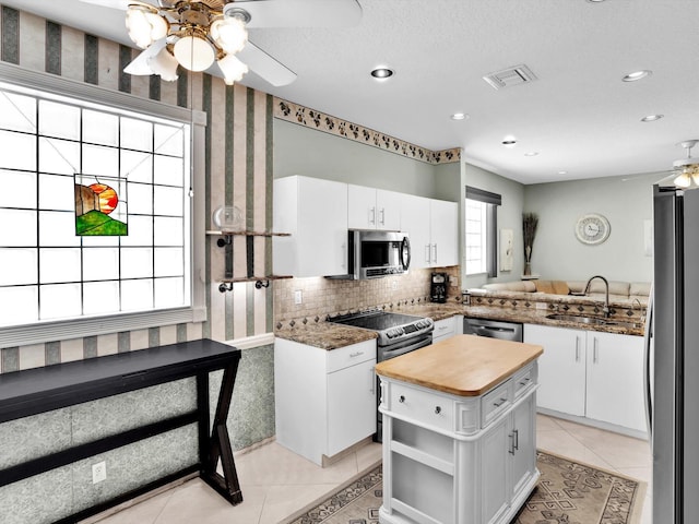 kitchen featuring kitchen peninsula, stainless steel appliances, ceiling fan, white cabinets, and a center island