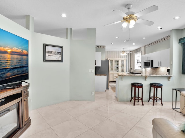 kitchen featuring white cabinetry, light stone counters, kitchen peninsula, a kitchen bar, and appliances with stainless steel finishes