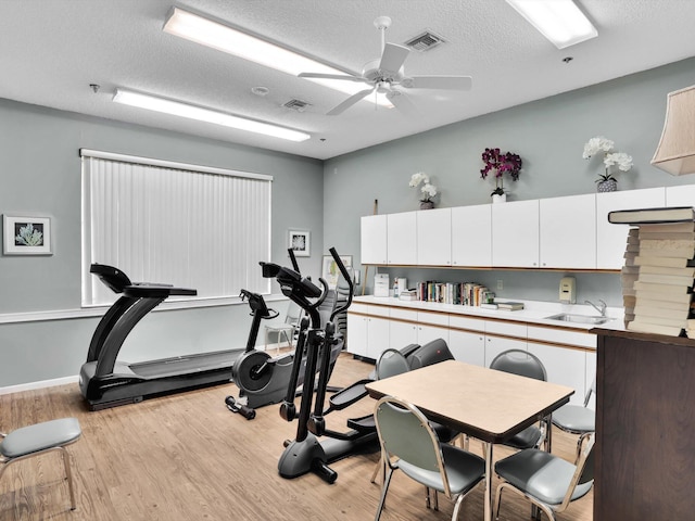 exercise area featuring a textured ceiling, ceiling fan, sink, and light hardwood / wood-style flooring