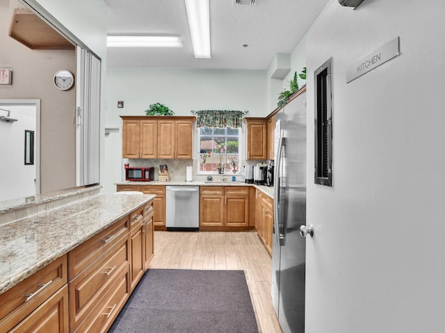 kitchen featuring appliances with stainless steel finishes, light wood-type flooring, light stone counters, a textured ceiling, and sink