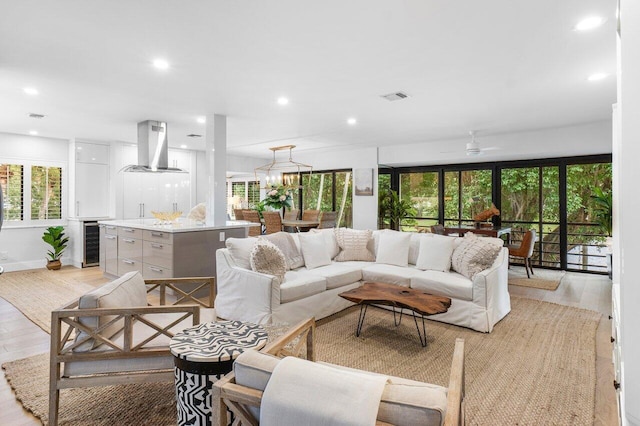 living room with ceiling fan with notable chandelier, wine cooler, and light hardwood / wood-style flooring