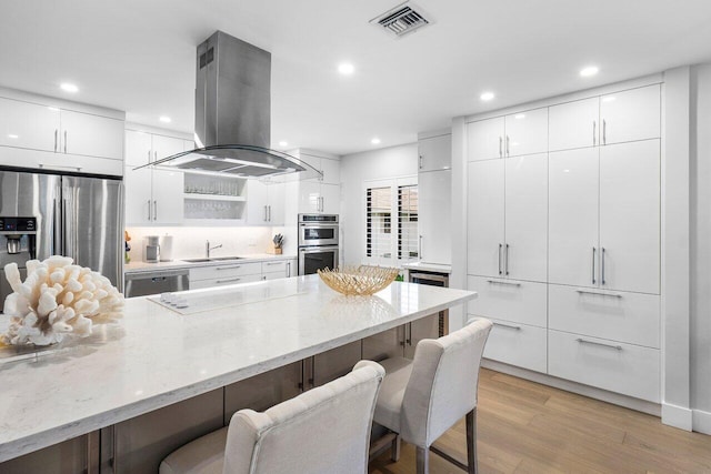 kitchen featuring a kitchen breakfast bar, island range hood, white cabinetry, and appliances with stainless steel finishes