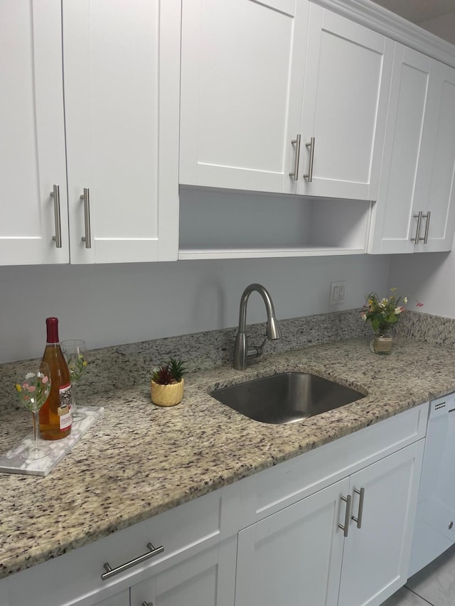 kitchen with light stone counters, white dishwasher, sink, light tile patterned floors, and white cabinetry