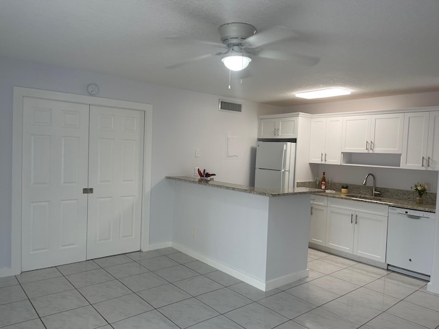 kitchen with white appliances, white cabinets, sink, light stone countertops, and kitchen peninsula