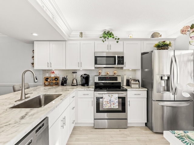 kitchen with appliances with stainless steel finishes, backsplash, light stone counters, sink, and white cabinetry