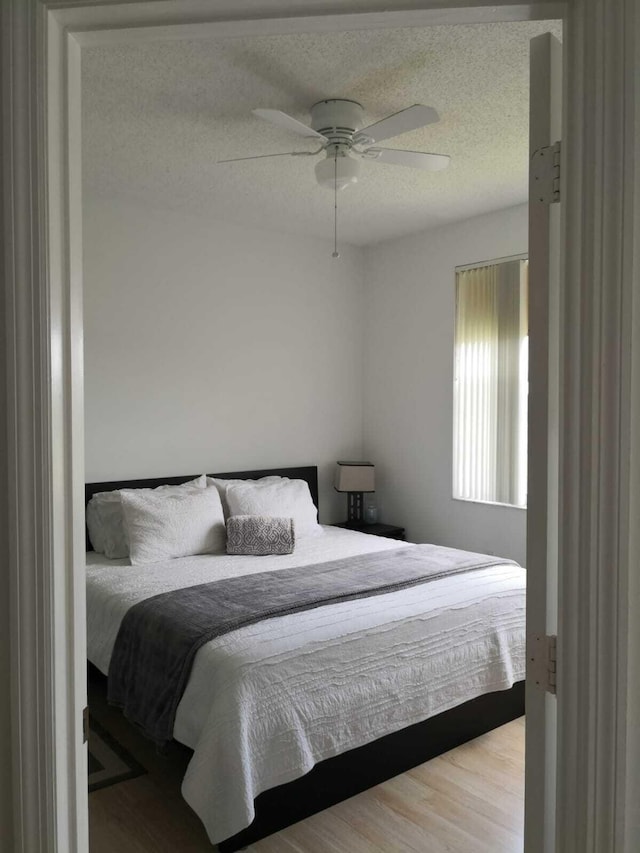 bedroom with ceiling fan, light hardwood / wood-style floors, and a textured ceiling