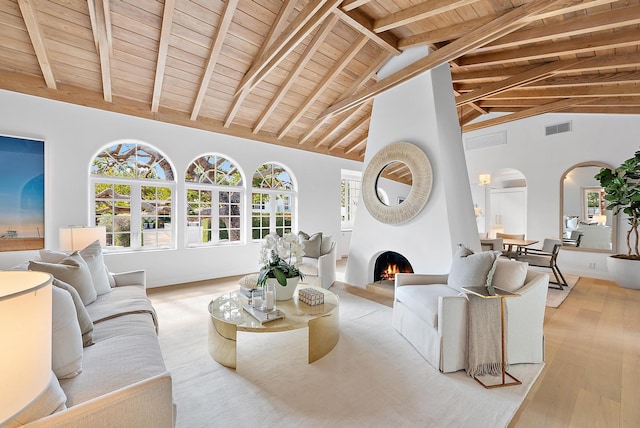 living room featuring a large fireplace, beam ceiling, high vaulted ceiling, light hardwood / wood-style flooring, and wooden ceiling