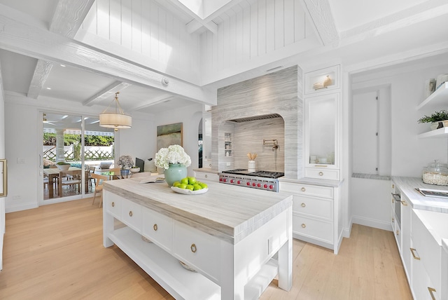 kitchen featuring pendant lighting, a center island, white cabinets, light wood-type flooring, and beamed ceiling