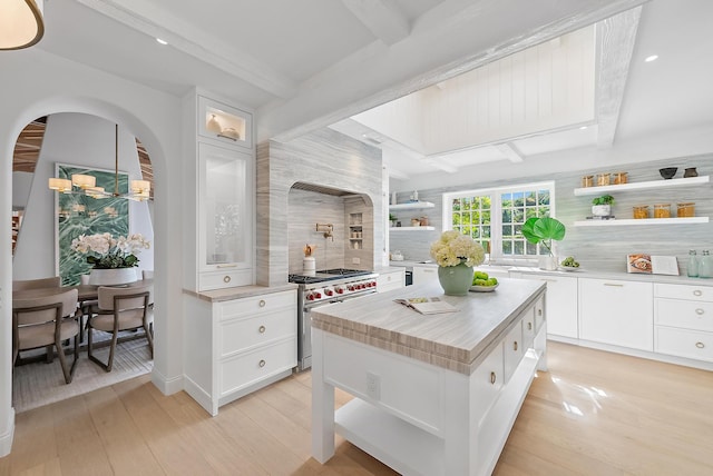 kitchen with a kitchen island, light wood-type flooring, white cabinetry, and stainless steel stove