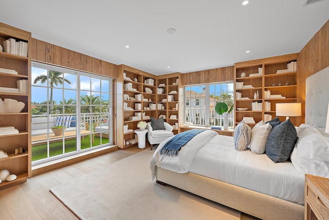 bedroom featuring multiple windows, wooden walls, and light wood-type flooring