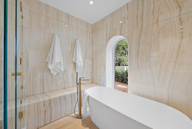 bathroom featuring a tub, hardwood / wood-style floors, and tile walls