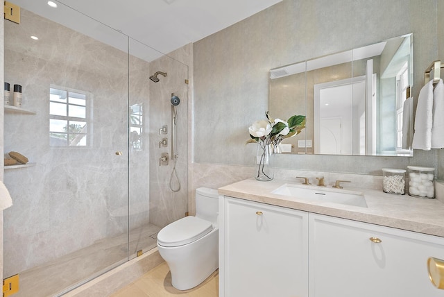 bathroom featuring tile patterned floors, toilet, a shower with door, vanity, and tile walls