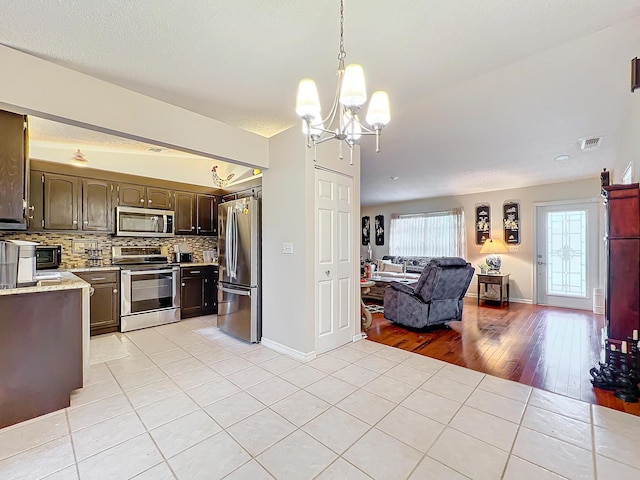 kitchen featuring stainless steel appliances, tasteful backsplash, a chandelier, decorative light fixtures, and light hardwood / wood-style floors