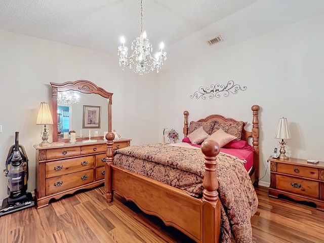 bedroom featuring a textured ceiling, light hardwood / wood-style floors, and an inviting chandelier