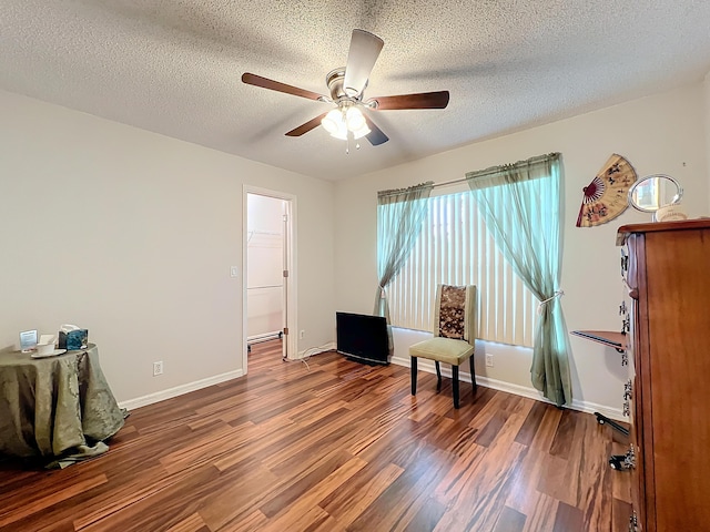 living area with a textured ceiling, baseboard heating, ceiling fan, and dark wood-type flooring