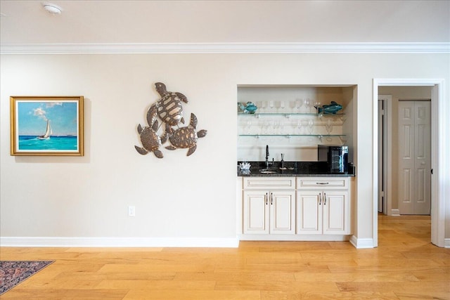 bar featuring crown molding, light hardwood / wood-style flooring, and dark stone counters