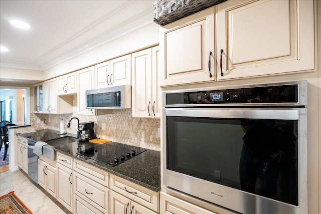 kitchen featuring sink, cream cabinets, dark stone counters, appliances with stainless steel finishes, and ornamental molding