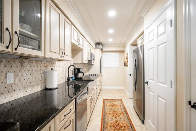 kitchen with decorative backsplash, dark stone countertops, ornamental molding, cream cabinetry, and stainless steel appliances