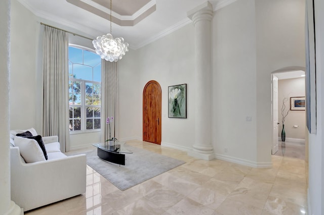 living area with an inviting chandelier, a raised ceiling, decorative columns, and ornamental molding