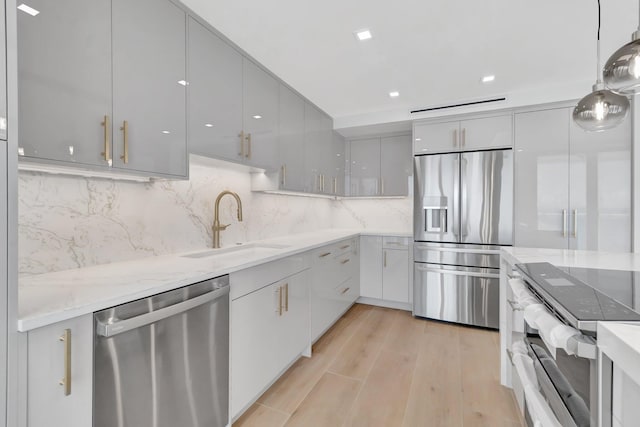 kitchen with sink, hanging light fixtures, light hardwood / wood-style flooring, appliances with stainless steel finishes, and tasteful backsplash