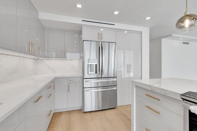 kitchen with hanging light fixtures, light stone counters, stainless steel fridge, light hardwood / wood-style floors, and white cabinets