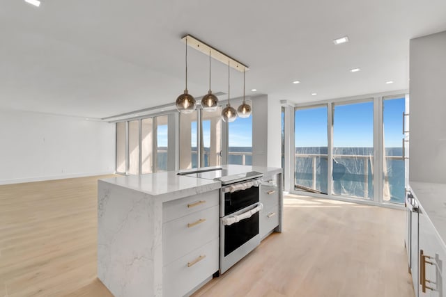 kitchen featuring white cabinets, hanging light fixtures, light wood-type flooring, an island with sink, and light stone counters