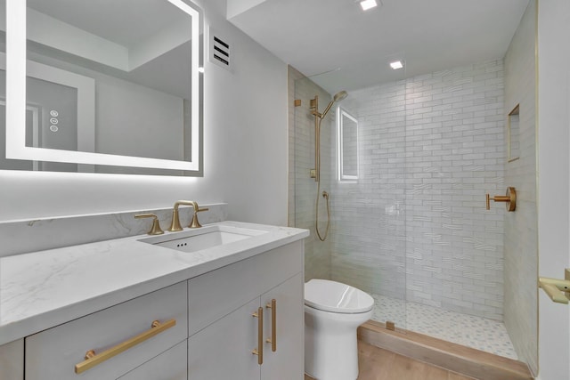 bathroom featuring a tile shower, vanity, toilet, and wood-type flooring