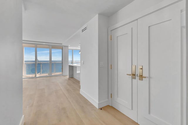 hallway with floor to ceiling windows, light hardwood / wood-style flooring, and a water view