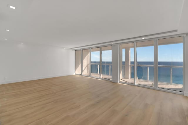 empty room with light wood-type flooring, a water view, and expansive windows