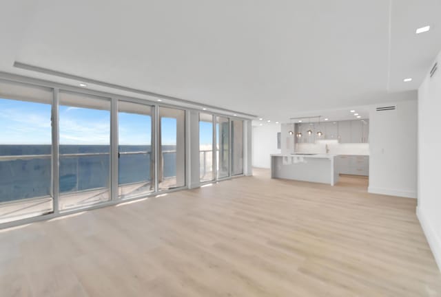 unfurnished living room with light hardwood / wood-style flooring, a water view, and a wall of windows