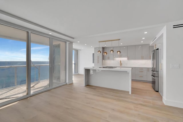 kitchen with decorative backsplash, stainless steel fridge, pendant lighting, a water view, and light hardwood / wood-style flooring