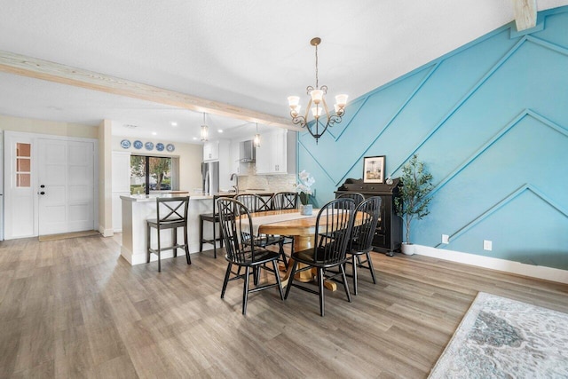 dining space featuring beamed ceiling, light hardwood / wood-style floors, a textured ceiling, and an inviting chandelier