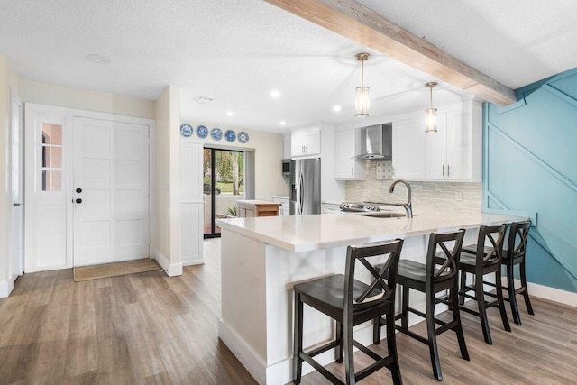 kitchen with kitchen peninsula, stainless steel appliances, wall chimney range hood, white cabinets, and hanging light fixtures