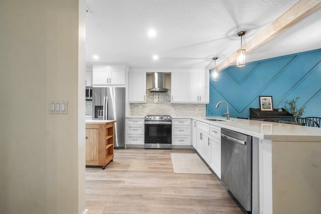 kitchen with white cabinets, wall chimney exhaust hood, pendant lighting, and appliances with stainless steel finishes