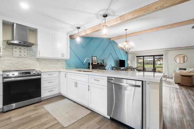 kitchen with pendant lighting, sink, wall chimney exhaust hood, white cabinetry, and stainless steel appliances