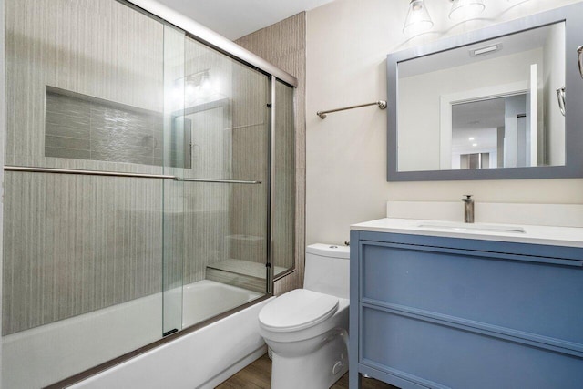 full bathroom featuring hardwood / wood-style flooring, vanity, combined bath / shower with glass door, and toilet