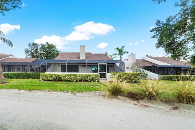 view of front of home featuring glass enclosure and a front yard