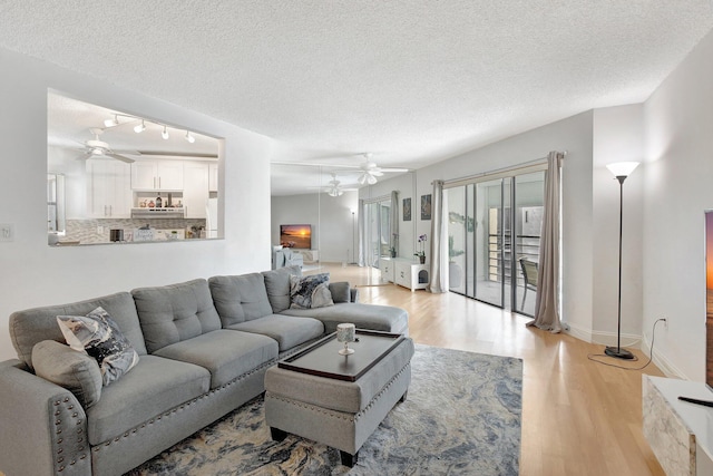 living room with ceiling fan, light hardwood / wood-style floors, and a textured ceiling