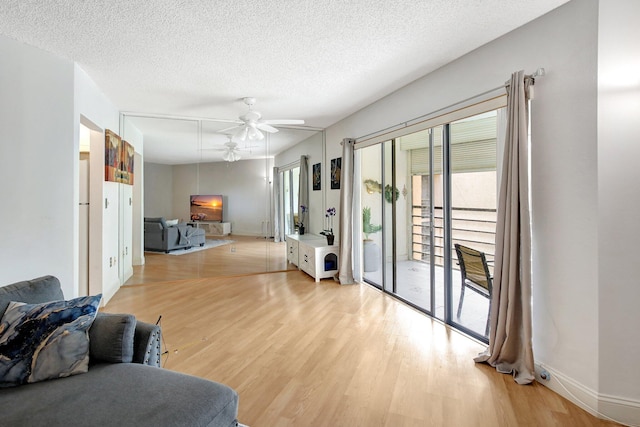 living room with ceiling fan, a textured ceiling, and light wood-type flooring