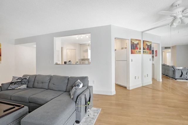 living room with ceiling fan, a textured ceiling, and light wood-type flooring