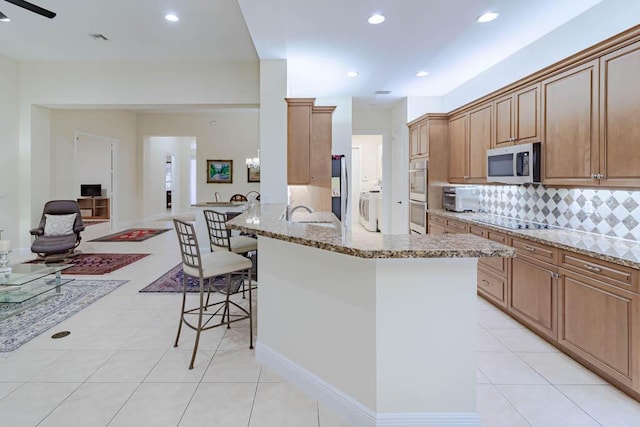 kitchen featuring a breakfast bar, tasteful backsplash, appliances with stainless steel finishes, light stone countertops, and washer / dryer